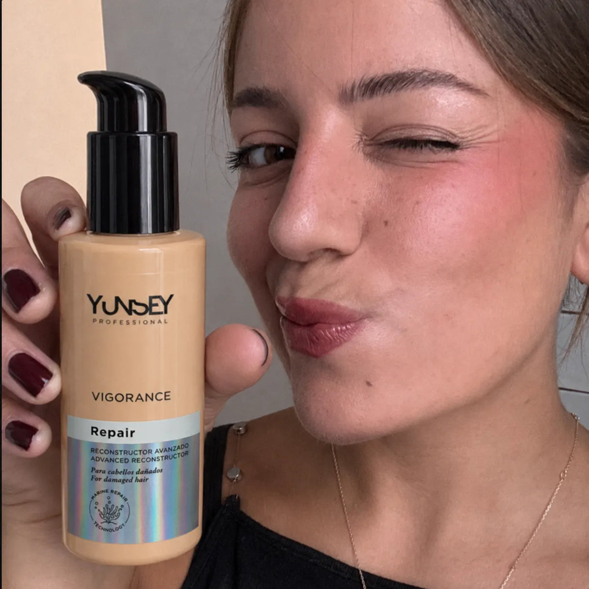 Mujer guiñando un ojo mientras sostiene un tratamiento reparador para cabello dañado disponible en PASABELU